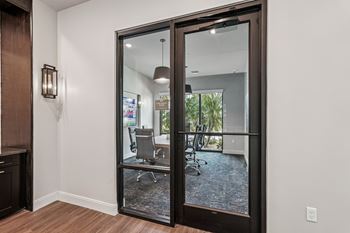 A glass door with a black frame leads to a room with a white wall and a brown cabinet